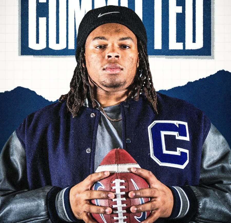 UConn signee in a letterman jacket holding a football